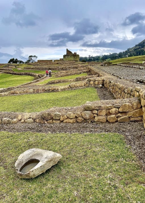 From the grassy foreground we look towards the distance passing over short stone walls that border grassy rooms that lead our eye to the sun temple of Ingapirca