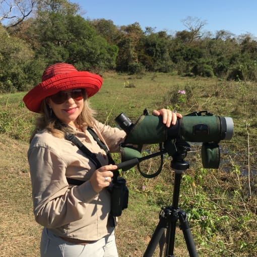 A woman in a bright red hat stands at a spotting scope