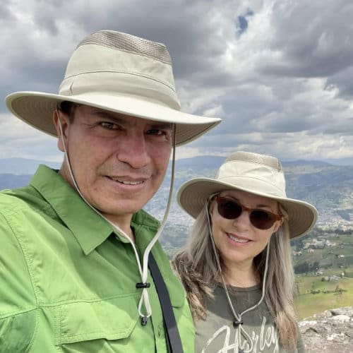 A man and woman pose for a selfie. Both are dressed for adventure in the Andes wearing caps with broad brims and comfortable outdoor wear.